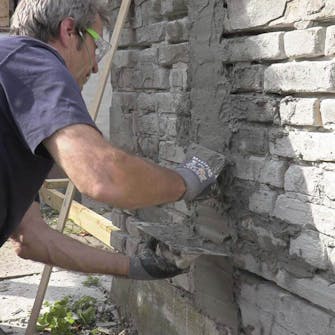 Mur med ødelagt puss og løse fuger: Påfør et lag med mørtel i en bred stripe Mur med ødelagt puss og løse fuger: Påfør et lag med mørtel i en bred stripe